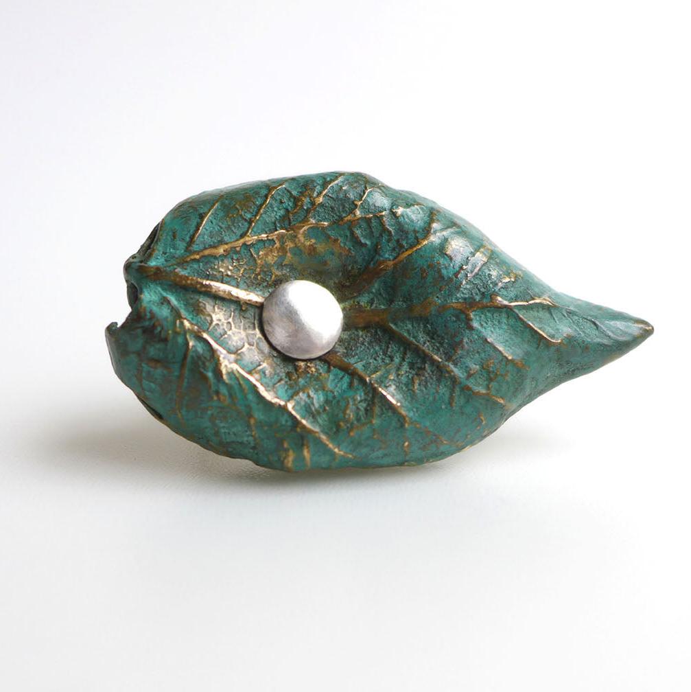 Cette bague est issue d'un moulage de feuilles d'arbres. Réalisée en bronze patiné au vert-de-gris, elle dévoile des détails délicats et texturés. Elle est rivetée au centre à un anneau en argent forgé.