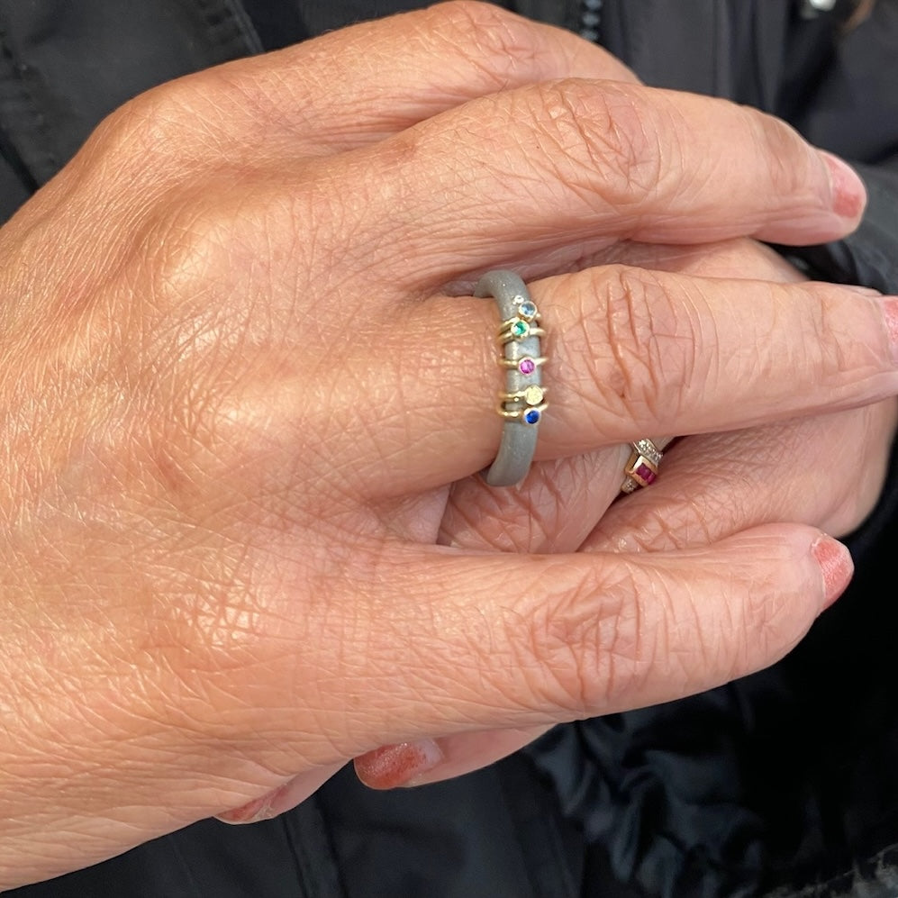 Bague en acier inoxydable ornée de 5 mini anneaux d'or. Chaque anneau est serti d'une pierre colorée. Mains croisées.