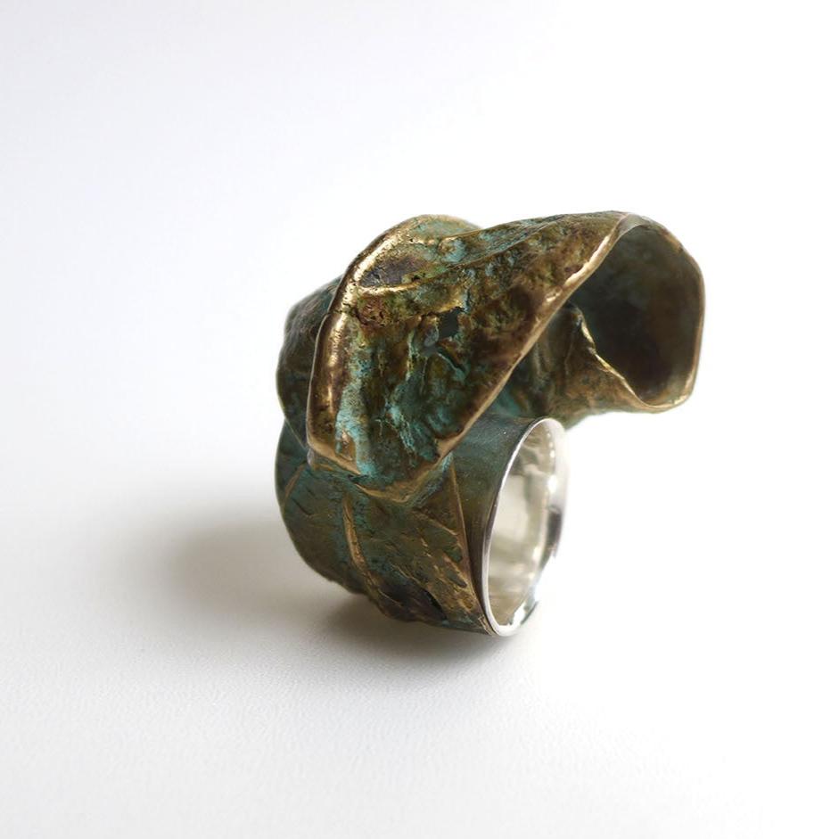 Bague sculpturale évoquant la nature avec une feuille d'arbre finement enroulée autour du doigt, comme une étreinte végétale. Réalisée en bronze patiné au vert-de-gris. Vue de profil sur fond blanc.