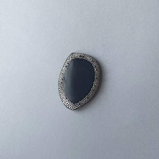 Broche unique en corne noire ornée d'une frise de 50 mm composée de points blancs peints à la main, rappelant le pointillisme de l'art aborigène. De mini perles d'hématites soulignent ce travail abstrait. 