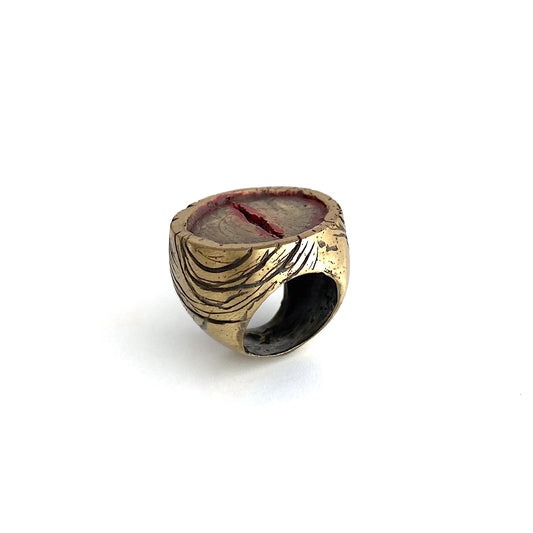 Chevalière sculpturale ronde en bronze , une entaillé au centre dans le métal est soulignée de peinture acrylique rouge.  Les flancs la bague sont griffés de noir.