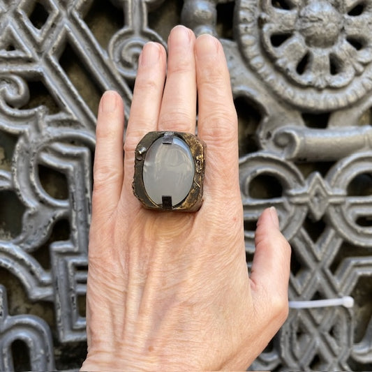 Bague Sculpturale rectangulaire en bronze patiné et texturé accueille une grande agate blanche ovale tenue par deux griffes de chaque côté. Bague portée, décor relief métalique.