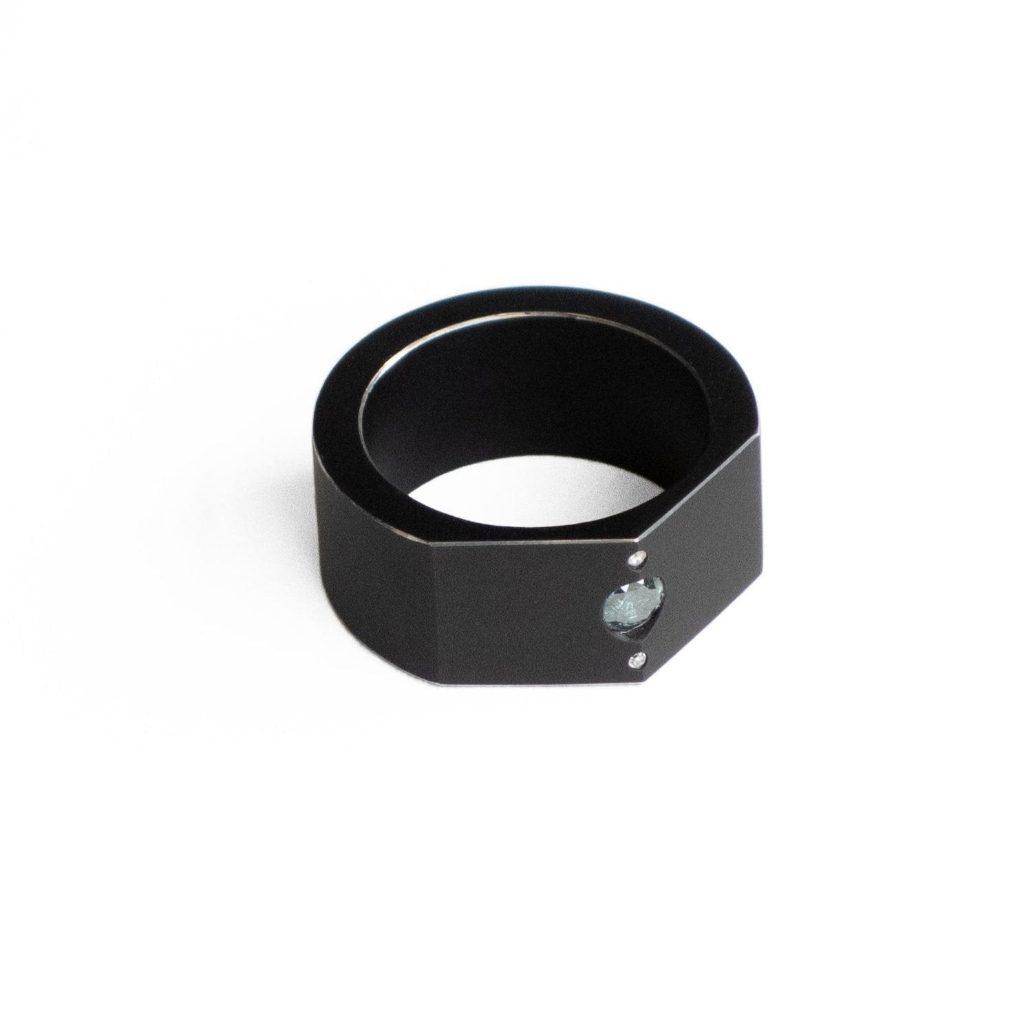 Bague graphique forme de chevalière en aluminium noir. Sur le dessus un diamant bleu est serti entre deux petits diamants blancs.