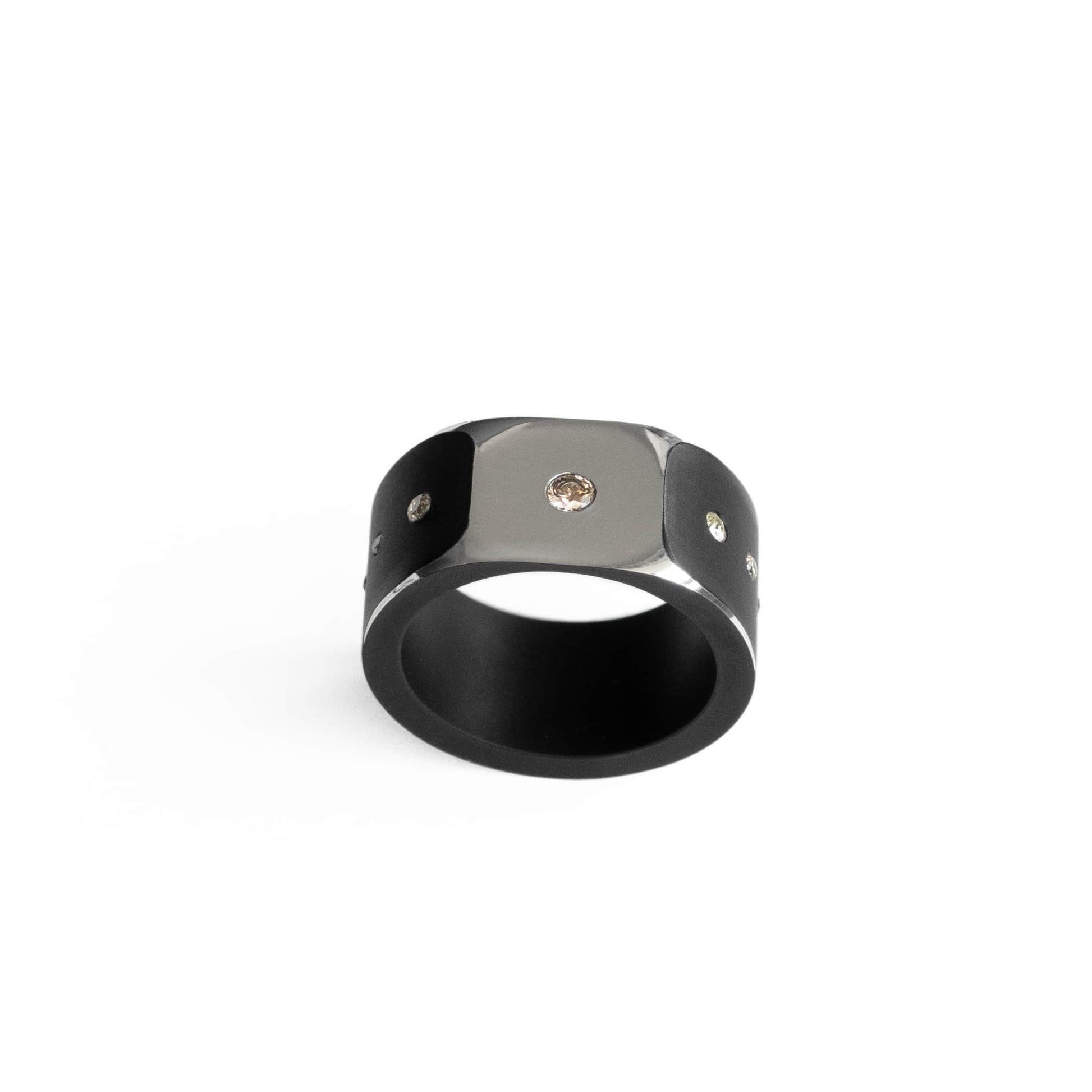 Bague forme chevalière en aluminium noir mat. Sur la surface polie miroir un diamant central est serti. Trois diamants dégradés ornent les deux côtés de l'anneau .