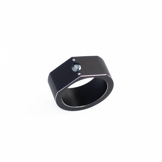 Bague graphique en aluminium noir en forme de chevalière . Sur le dessus un diamant bleu est serti entre deux petits diamants.