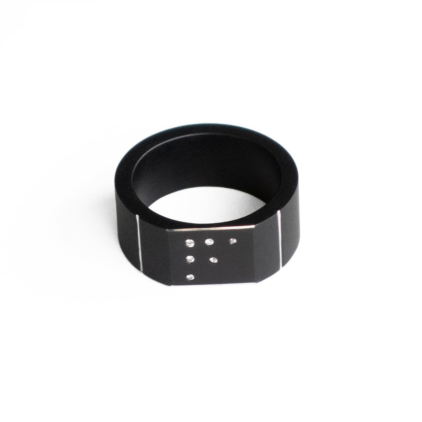 Bague moderne forme chevalière en aluminium anodisé noir mat, fini par trois filets polis miroir. Sur la surface plane du bijou, six petits diamants blancs sont sertis en dégradé.