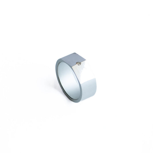 Bague biseautée en forme de chevalière, en aluminium anodisé gris. Son design met en valeur le contraste des finition mates et brillantes du métal. Au sommet un diamant blanc est serti.