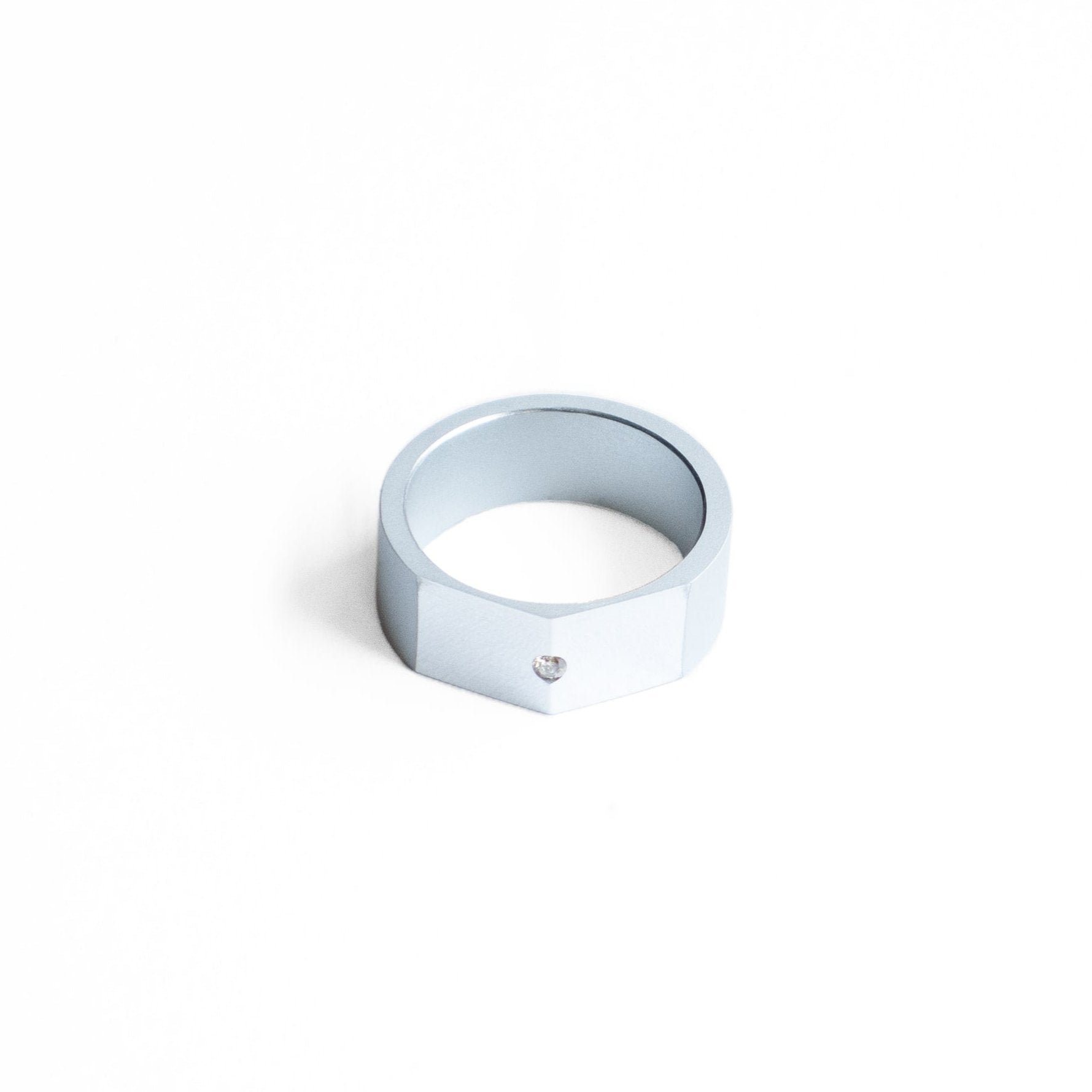 Bague style chevalière, en aluminium anodisé gris.Son design met en valeur le contraste des finition mates et brillantes du métal. Sur le sommet  biseauté et poli sur trouve un diamant blanc.