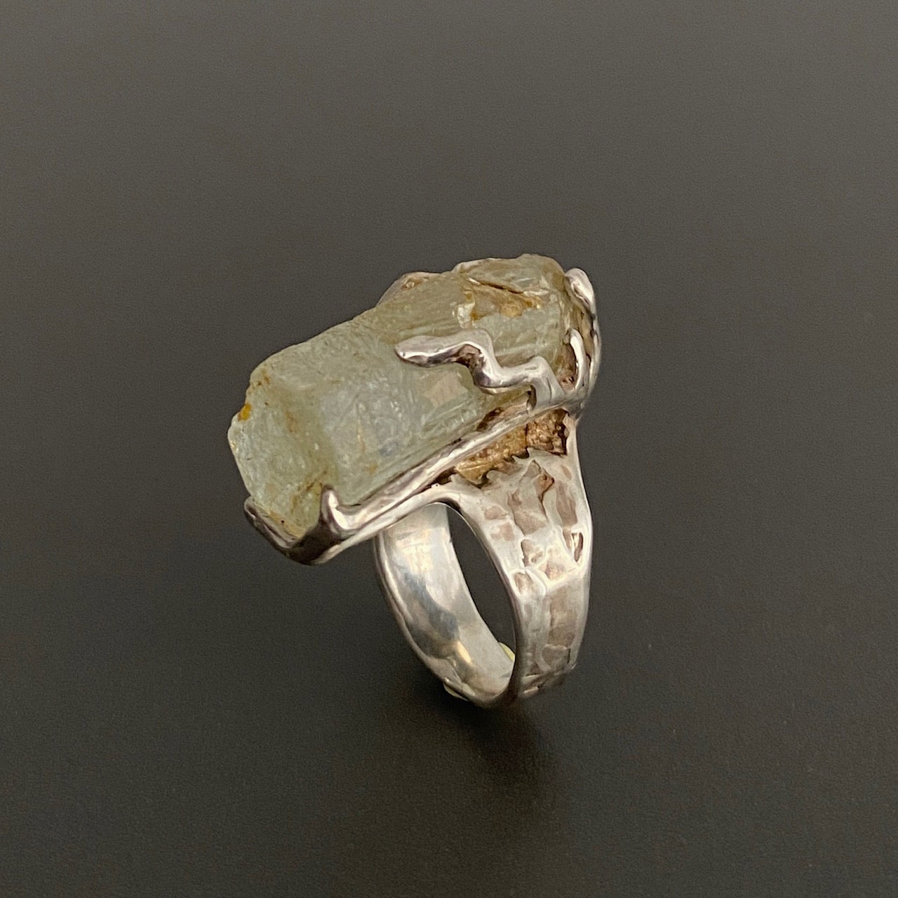 Bague sculpturale en argent ornée d’une Aigue-marine hexagonale sur fond gris.