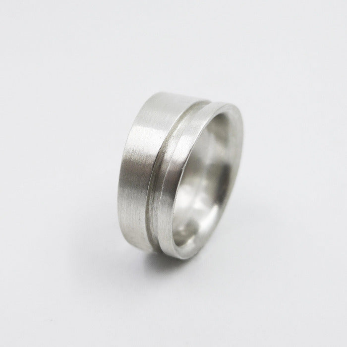 Bague pour homme et femme en argent brossé. Un fin liseré creusé dans le métal confirme l'asymétrie et la sobriété du design